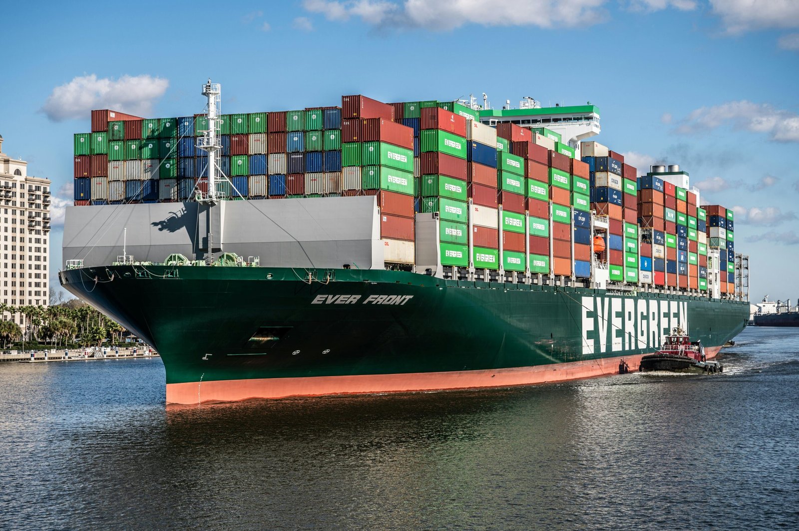 A large container ship, the Ever Front, being guided by a tugboat in a busy seaport.